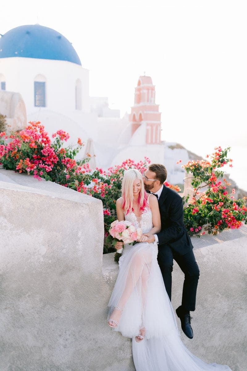 A couple embracing on a bougainvillea-draped terrace in Santorini, Greece, a Scheme Events destination wedding
